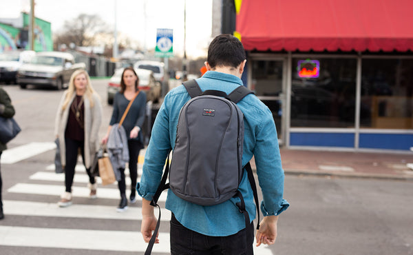 A person carrying their Luminary 15 via the backpack straps at a crosswalk.